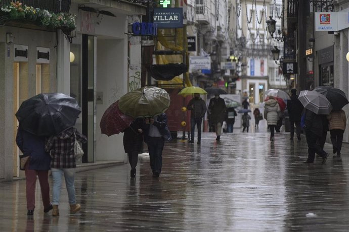 Transeúntes caminan protegidos por una vía de A Coruña