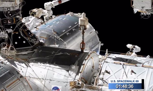 Dos astronautas trabajan en el exterior de la Estación Espacial sujetos al brazo robótico