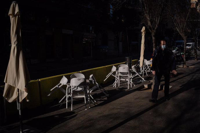 Un hombre pasa al lado de las sillas vacías de una terraza en Barcelona, Catalunya (España).