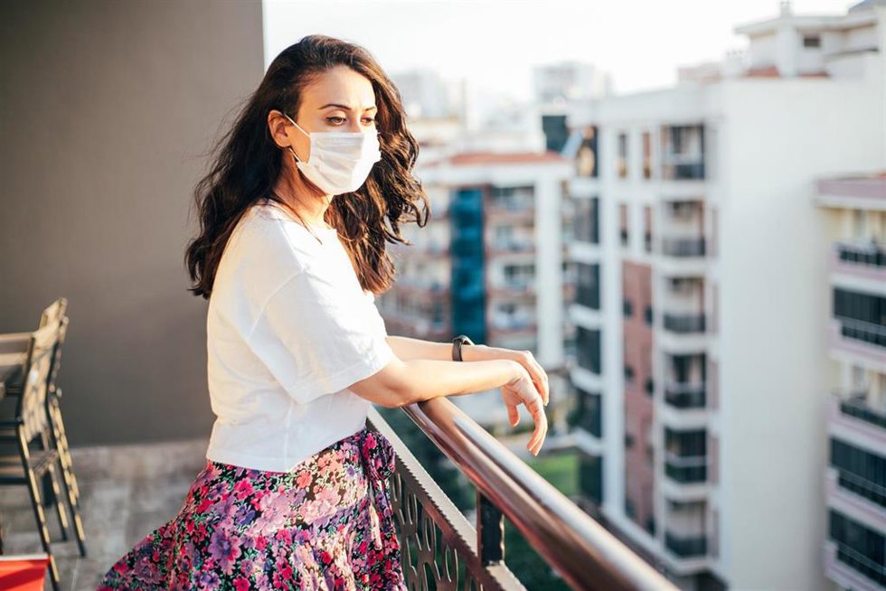 Mujer con mascarilla mira desde el balcón durante el confinamiento por el coronavirus.
