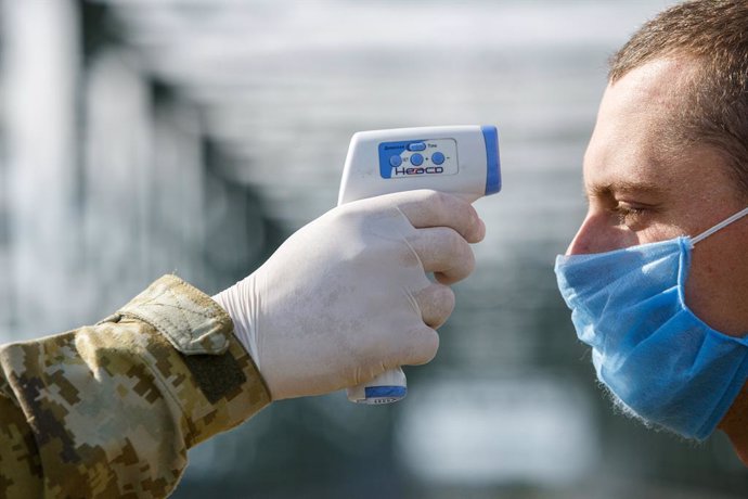 20 May 2020, Ukraine, Chop: A border guard personnel measures a man's body temperature at the Tysa international automobile checkpoint on the Ukraine-Hungary border during the coronavirus quarantine. Photo: -/Ukrinform/dpa