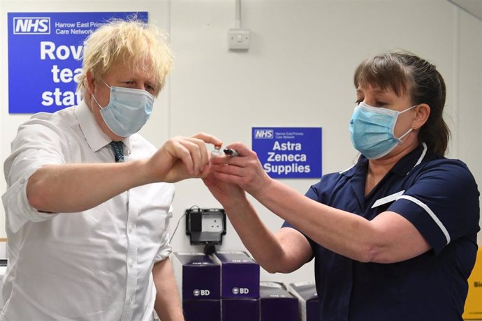 25 January 2021, United Kingdom, London: UK Prime Minister Boris Johnson (L) is shown a vial of the Oxford/Astrazeneca COVID-19 vaccine during a visit to Barnet FC's ground at The Hive, which is being used as a coronavirus vaccination centre.
