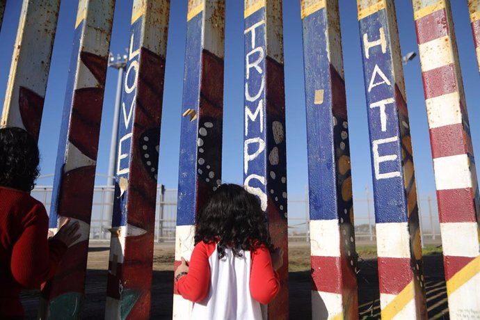 Una niña mira hacia los Estados Unidos a lo largo de la valla fronteriza entre Estados Unidos y México.