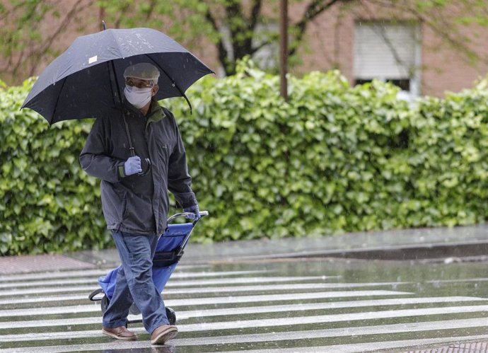 Transeúntes protegidos con mascarilla y un paraguas caminan por las calles de la capital un día marcado por la llegada a la península de una borrasca fría que ha activado la alerta por viento o lluvia en 8 comunidades, entre ellas, Madrid
