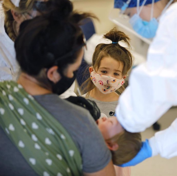 Una niña con mascarilla observa como atienden a su hermano en un centro sanitario de California