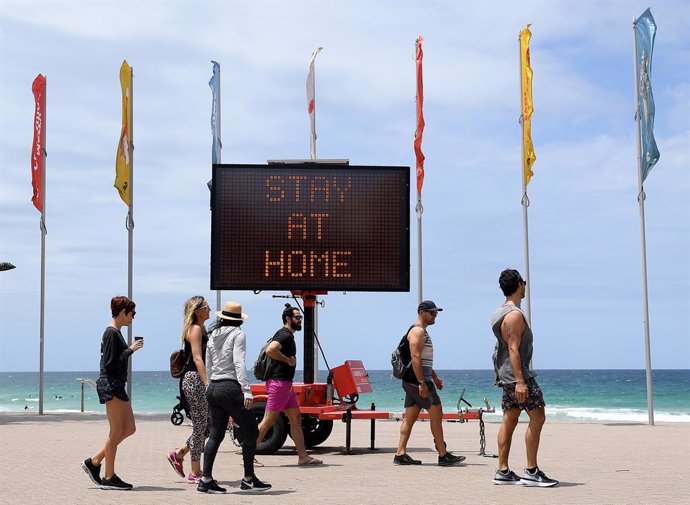 26 December 2020, Australia, Sydney: People walk in front of an electronic board written on it "Stay at Home" on the empty Manly beach. Sydney's northern beaches remain under New South Wales Government (NSW) ordered lockdown as the Government tries to c