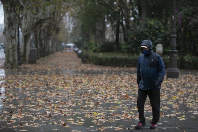 Una persona camina protegido del viento y la lluvia en Sevilla