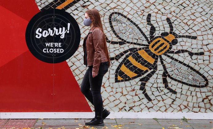 20 October 2020, England, Manchester: A person wearing a face mask walks past a poster of the Manchester Bee in Albert Square as the Government is preparing to impose stringent new coronavirus controls on 2.8 million people after talks with the local le