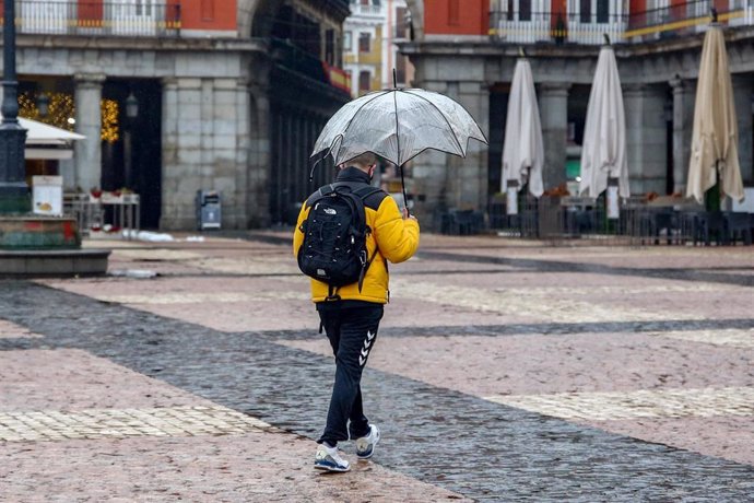 Un hombre camina protegido por un paraguas el mismo día de la llegada del temporal Gaetán, en la Plaza Mayor de Madrid, (España), a 20 de enero de 2021.