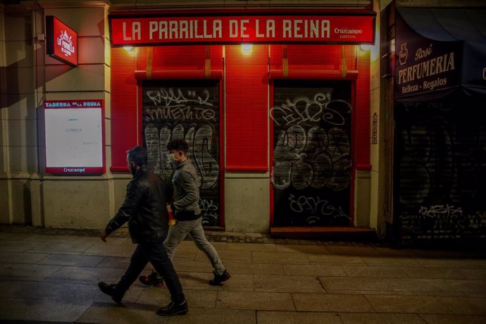 Dos jóvenes pasan por delante de un restaurante cerrado durante el primer día del toque de queda a las 10 de la noche, en Madrid (España), a 25 de enero de 2021. La Comunidad de Madrid amplía desde hoy el horario de las restricciones de movilidad noctur