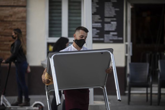 Un camarero recoge el mobiliario de la terraza de un bar