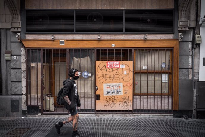 Un joven pasea al lado de un comercio tapiado en una de las principales calles de Buenos Aires.
