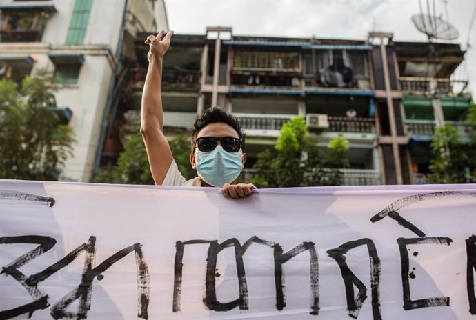05 February 2021, Myanmar, Yangon: A protester flashes the three fingers salute while holding a banner during the demonstration against the military coup in Myanmar. Myanmar's military seized power on 1 February 2021 and detained government officials in