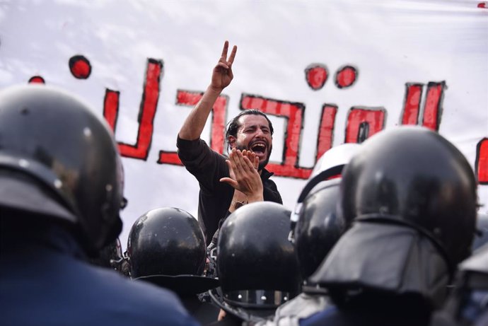 06 February 2021, Tunisia, Tunis: Aprotester flashes the victory sign in front of police personnel during an anti-government demonstration against police repression on the 8th anniversary of the assassination of leftist opposition leader Chokri Belaid.