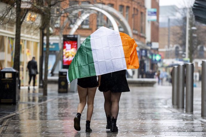 17 March 2020, Northern Ireland, Belfast: Two young girls shelter under the Irish flag as they walk through Belfast on St Patrick's Day. Due to Coronavirus Belfast City Council cancelled the festivities for the safety of the general public. Photo: Liam 