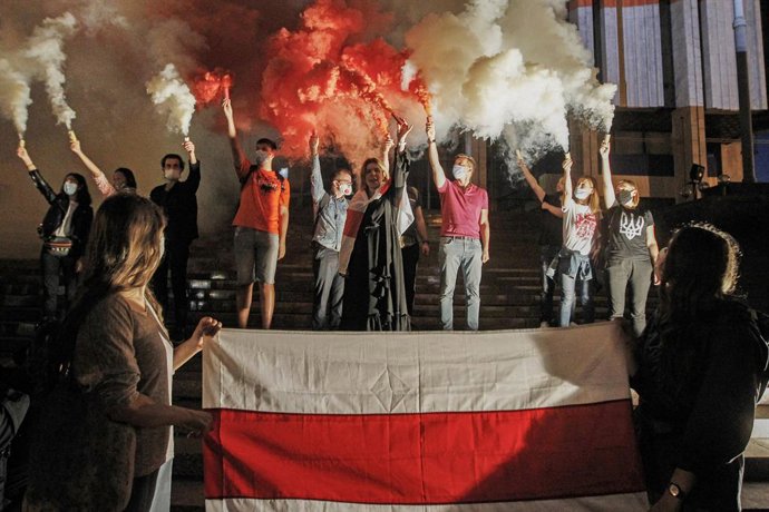 26 August 2020, Ukraine, Kiev: Members of the Belarusian community in Ukraine and Ukrainian activists burn red and white smoke bombs and wave the flag of the Rada of the Belarusian Democratic Republic (the Belarusian opposition flag) during rally in sol