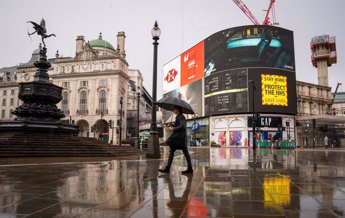 29 January 2021, United Kingdom, London: A man with an umbrella walks past a government coronavirus advert on the big screen at Piccadilly Circus during England's third national lockdown to curb the spread of coronavirus. Photo: Dominic Lipinski/PA Wire