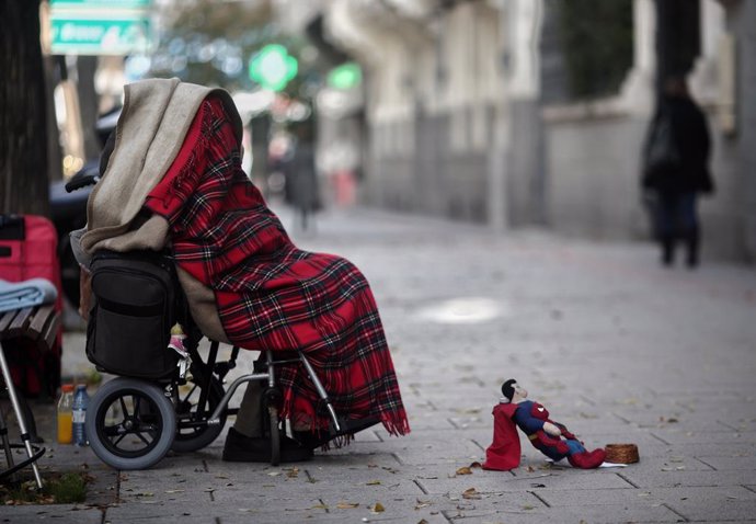 Una persona en silla de ruedas y tapada con una manta pide dinero con un muñeco de Superman en una céntrica calle durante la segunda ola de la pandemia del coronavirus, en Madrid (España), a 18 de noviembre de 2020.