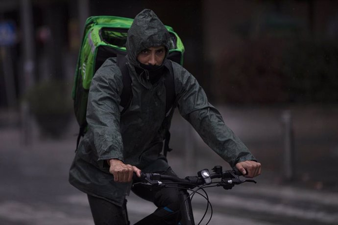 Un rider (repartidor) trabaja bajo la lluvia protegido con un impermeable. En Sevilla (Andalucía, España), a 04 de diciembre de 2020.