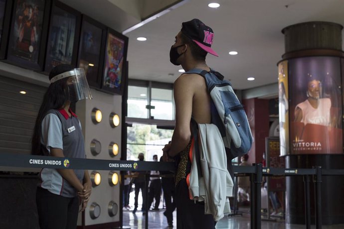 Un hombre con mascarilla hablando con la trabajadora de un cine en Venezuela