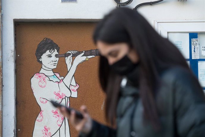 Una mujer consulta su smartphone al pasar frente a un mural de una mujer con un catalejo en Lugo, tras el levantamiento del cierre perimetral de la ciudad, en Lugo, Galicia (España), a 30 de diciembre de 2020.  Lugo y Ourense serán las dos únicas urbes 