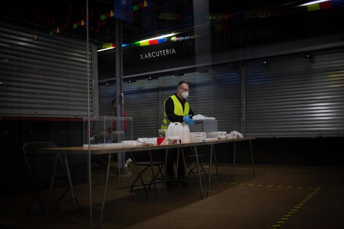 Un operario coloca las urnas, papeletas, gel desinfectante y demás material electoral en una mesa del Mercat del Ninot
