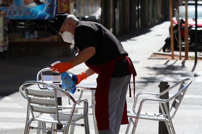 Un camarero limpia las mesas y sillas de una terraza de un bar 
