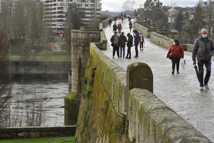 Varias personas caminan por el puente Romano a su paso por el río Miño, en Ourense, Galicia (España), a 11 de febrero de 2021. El volumen del Miño a su paso por la ciudad presentó ayer un elevado volumen, de hasta 5,34 metros, superando el nivel de acti