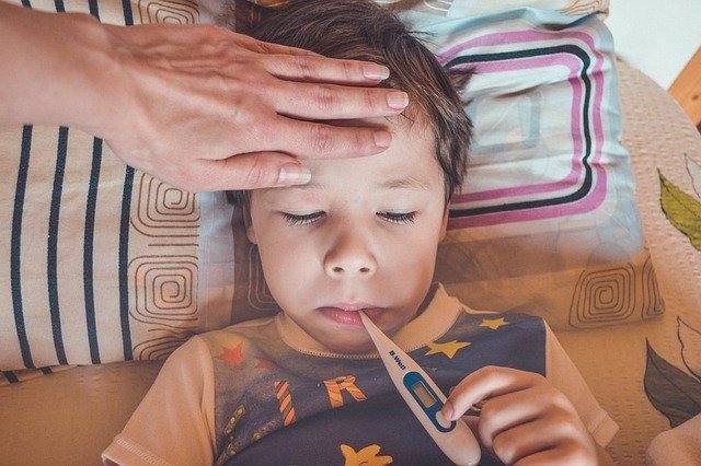 Niño enfermo con tomándose la temperatura con un termómetro.