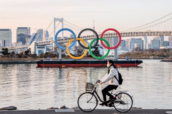 25 January 2021, Japan, Tokyo: A woman wears a face mask while riding a bicycle past the Olympic logo in Odaiba. Photo: Viola Kam/SOPA Images via ZUMA Wire/dpa