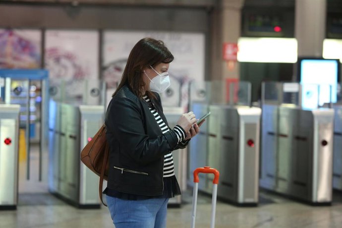 Una viajera con mascarilla consulta su móvil en la estación de Atocha (Madrid)