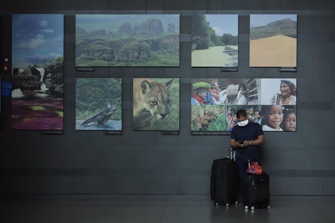 Un hombre con mascarilla espera con maletas frente al aeropuerto de Bogotá, Colombia.