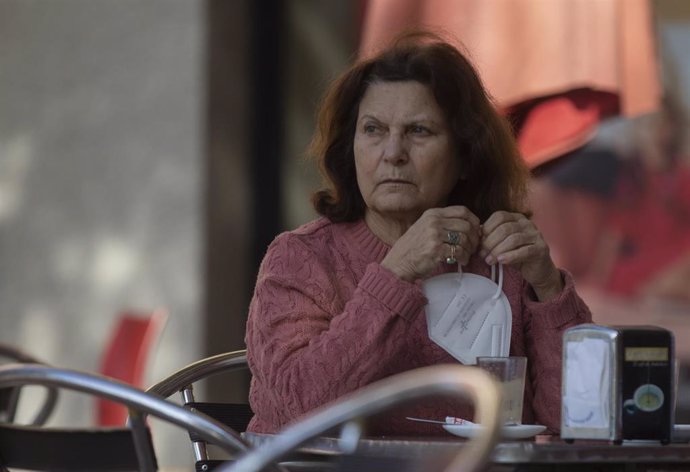 Una mujer en la terraza de un bar con la mascarilla en la mano, mientras continúa el cierre perimetral en Montequinto (Dos Hermanas), al entrar en nivel 4 de alerta  desde el pasado 20 de enero cuando superó la tasa de incidencia de Covid-19 de 500 caso