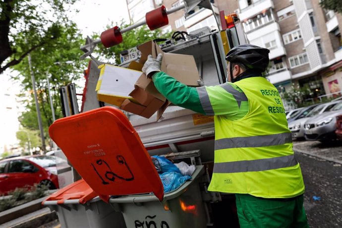 Un operario de recogida de residuos protegidos con mascarilla extrae cajas de cartón de un cubo de basura para triturarlas en un camión de basura durante su trabajo de limpieza en una calle de la capital durante el día 33 del estado de alarma, en Madrid