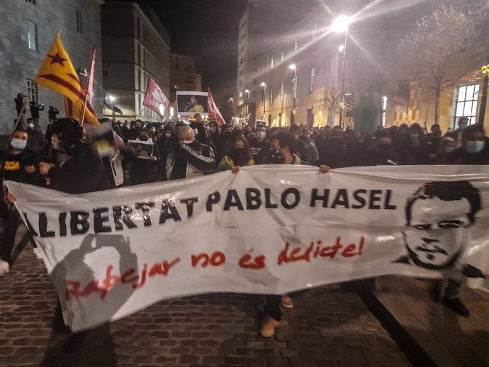 Varias personas sujetan una pancarta en la que se lee: `Libertat Pablo Hasel en una concentración de más de 2.000 personas en rechazo al encarcelamiento de Pablo Hasel por las calles de Girona, Cataluña (España), a 16 de febrero de 2021.