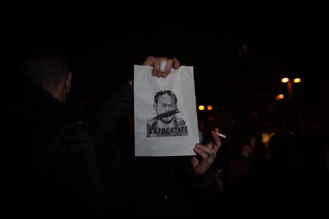 Un hombre sujeta un cartel en que se ve la cara de Pablo Hasel y `llibertat durante una concentración en rechazo al encarcelamiento de Pablo Hasel en la plaça Lesseps en Barcelona, Cataluña (España), a 16 de febrero de 2021