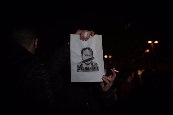Un home subjecta un cartell en qu es veu la cara de Pablo Hasel i `llibertat durant una concentració en rebuig a l'empresonament de Pablo Hasel en la plaa Lesseps a Barcelona, Catalunya (Espanya), a 16 de febrer de 2021
