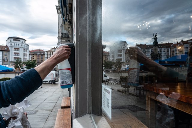 Una camarera limpia el cristal de su cafetería , en Vitoria, Álava, País Vasco