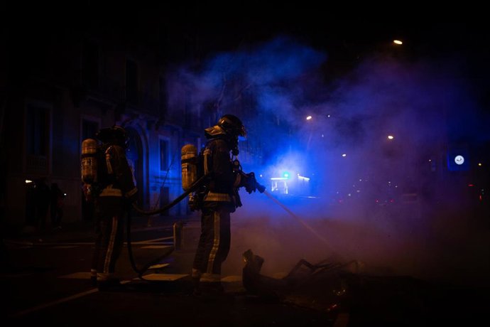 Bomberos apagan un incendio provocado por los manifestantes que apoyan a Pablo Hasel durante los disturbios en Barcelona (España), a 17 de febrero de 2021. El rapero Pablo Hasel ingresó la mañana de ayer martes en el centro penitenciario de Ponent, en L