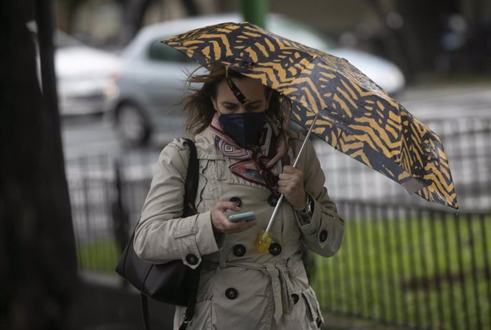 Una mujer camina bajo su paraguas durante un día lluvioso y con rachas de viento.