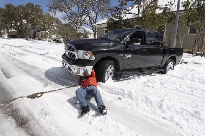 15 February 2021, US, Austin: A motorist tries to hook a chain to his truck stuck for several hours in downtown Austin after a rare snowstorm overnight in central Texas. Austin is shut down waiting for a temperature rise later this week. Photo: Bob Daem