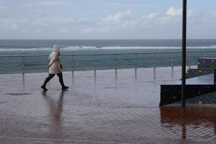 Una mujer camina bajo la lluvia en un paseo marítimo.