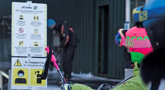 Dos esquiadors consulten la mesures de seguretat a l'estació d'esquí de La Molina (Girona) per evitar contagis de covid-19.