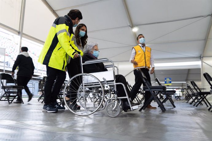 03 February 2021, Chile, Santiago: Leonila Gonzalez, 96, is taken by municipal personnel to the vaccination booth on the first day of mass vaccination, at a vaccination centre mounted at the Bicentenario Stadium. Photo: Matias Basualdo/ZUMA Wire/dpa