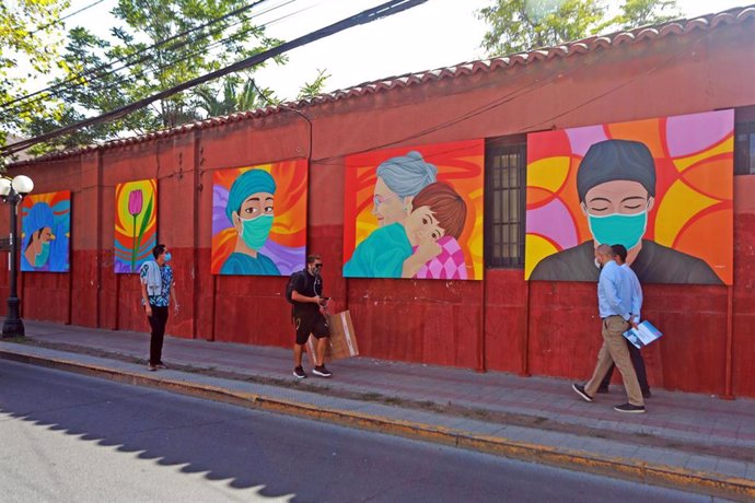 Varias personas caminan al lado de 30 murales realizados en Santiago de Chile por el artista Sebastián Durán para reconocer el esfuerzo de los chilenos contra la pandemia.