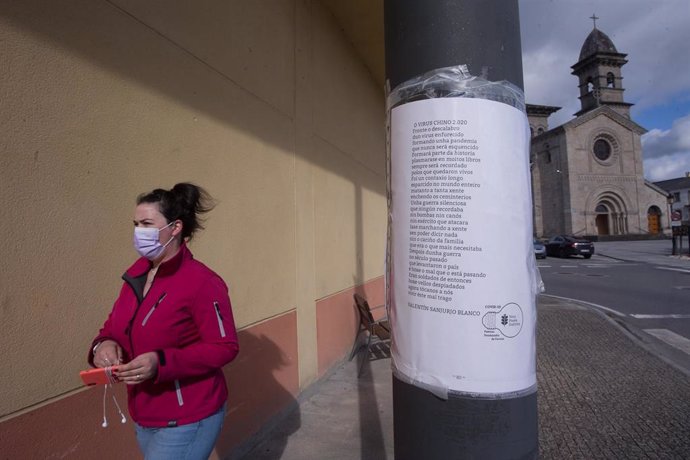 Una mujer camina frente a una farola donde hay pegado un papel con un poema titulado 'El virus chino 2020', en el municipio gallego de Guitiriz, en Lugo, Galicia (España), a 17 de febrero de 2021