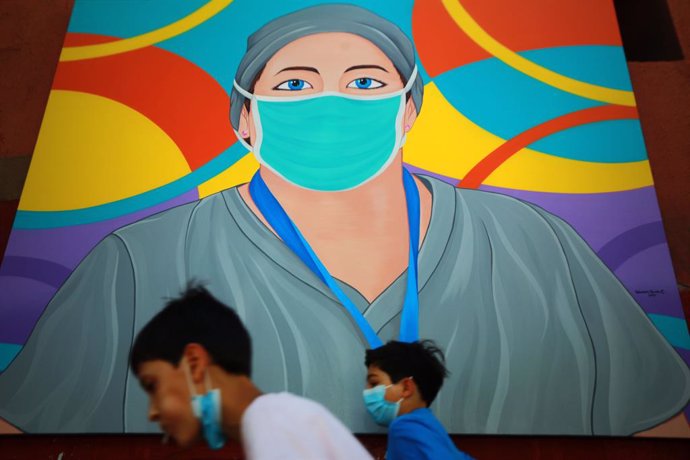 25 February 2021, Chile, Santiago: Children walk past one of more than 30 paintings made by the artist Sebastian Duran recognising the ongoing efforts of the Chilean frontline services during the coronavirus pandemic. Photo: Jose Francisco Zuniga/Agenci