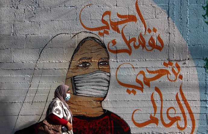 27 February 2021, Palestinian Territories, Gaza: A Palestinian woman walks past a mural in Gaza city. Photo: Mahmoud Ajjour/APA Images via ZUMA Wire/dpa