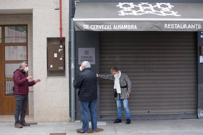 Dos personas conversan frente a un bar con las persianas bajadas en el municipio de Guitiriz, Galicia.