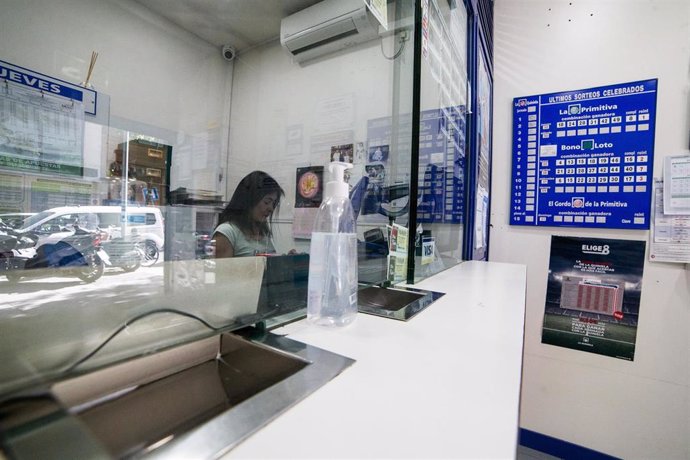 Archivo - Una dependienta trabaja en el interior de una administración de lotería de la capital con gel desinfectante para los clientes.